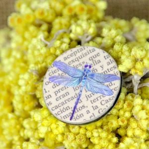 Bague en papier comprenant un disque de papier sur lequel est collé la page d'un livre. Et au dessus une libellule aux tons violets.